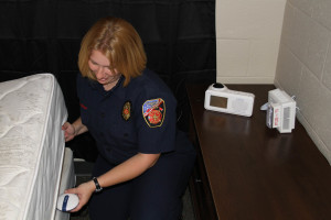 Fire Prevention Training Officer Laura Coleman places a bed shaker unit designed to alert a hearing impaired person of smoke or fire.
